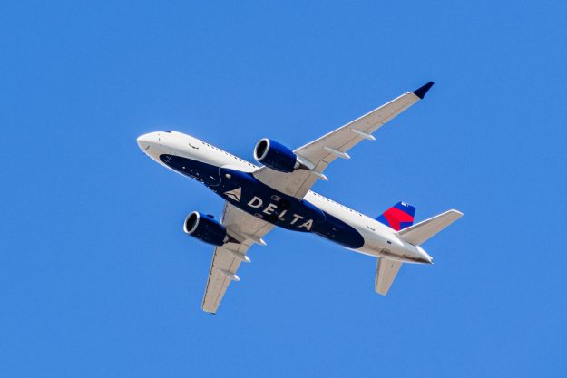 An airplane flying directly above with "DELTA" written on the bottom of the plane. August 1, 2019 Santa Clara / CA / USA - Delta Airlines aircraft in flight; the Delta Logo visible on the airplanes' underbelly; blue sky background
